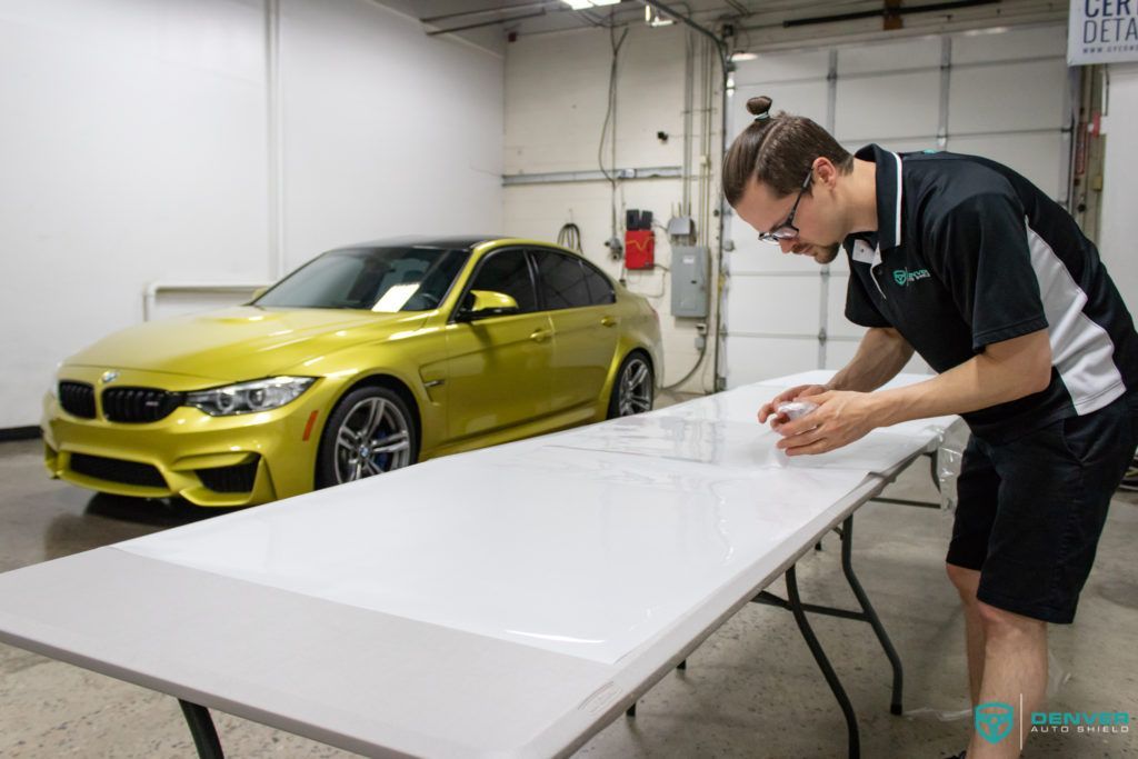 A man is working on a table in front of a yellow bmw m3.