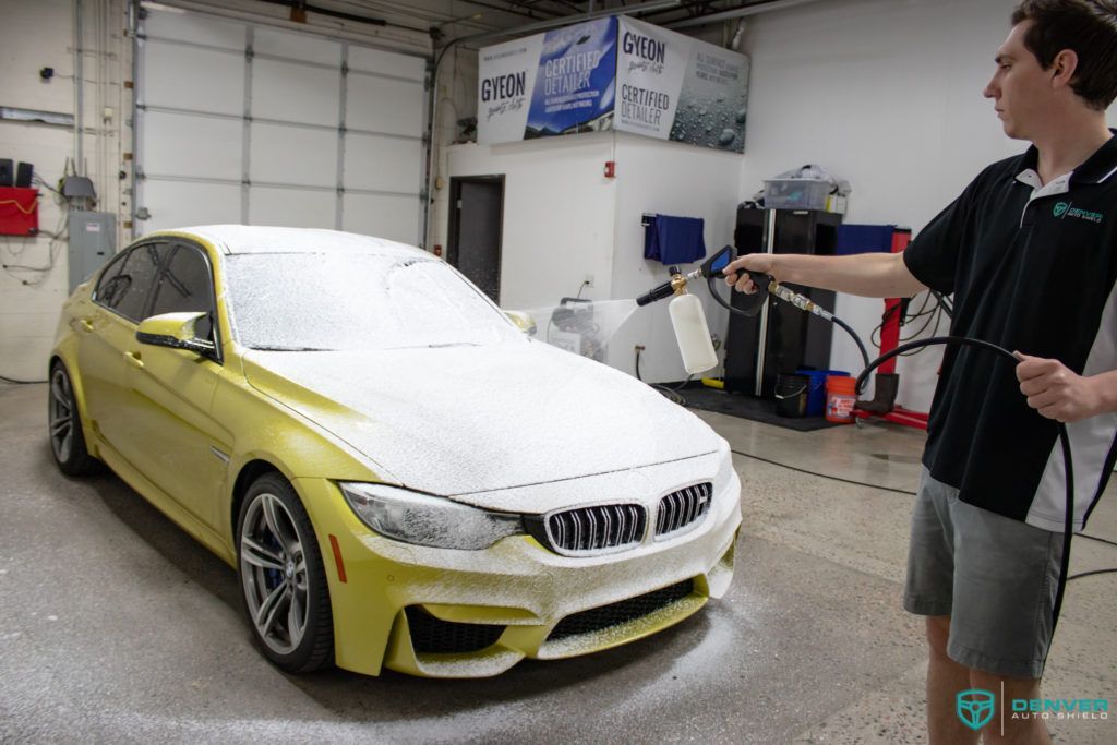 A man is washing a yellow bmw m3 in a garage.