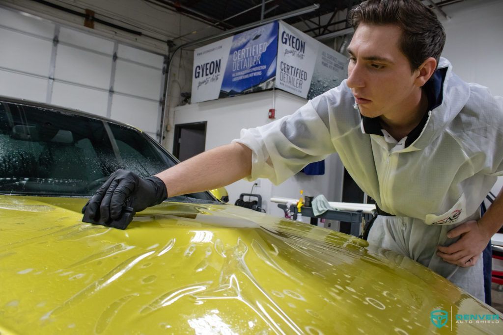 A man is cleaning the hood of a yellow car.