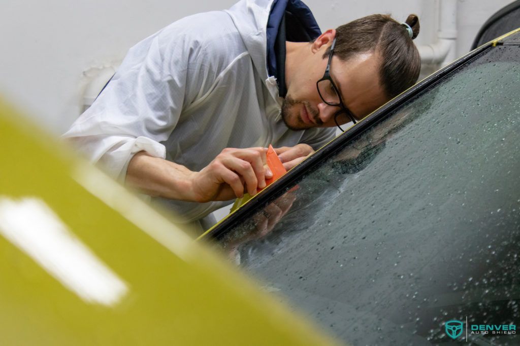 A man wearing glasses is cleaning the windshield of a car.