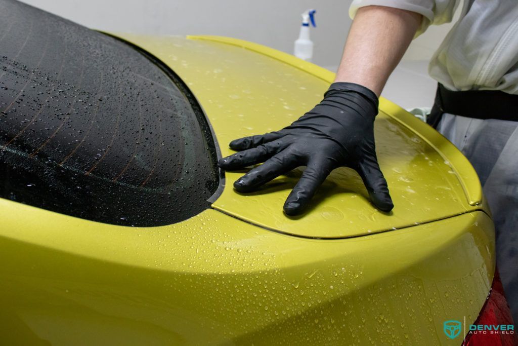 A person wearing black gloves is washing a yellow car.