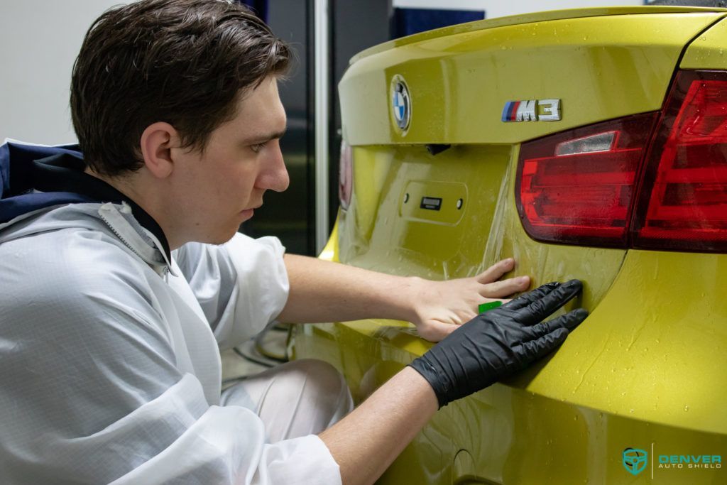 A man is cleaning the back of a yellow bmw m3.