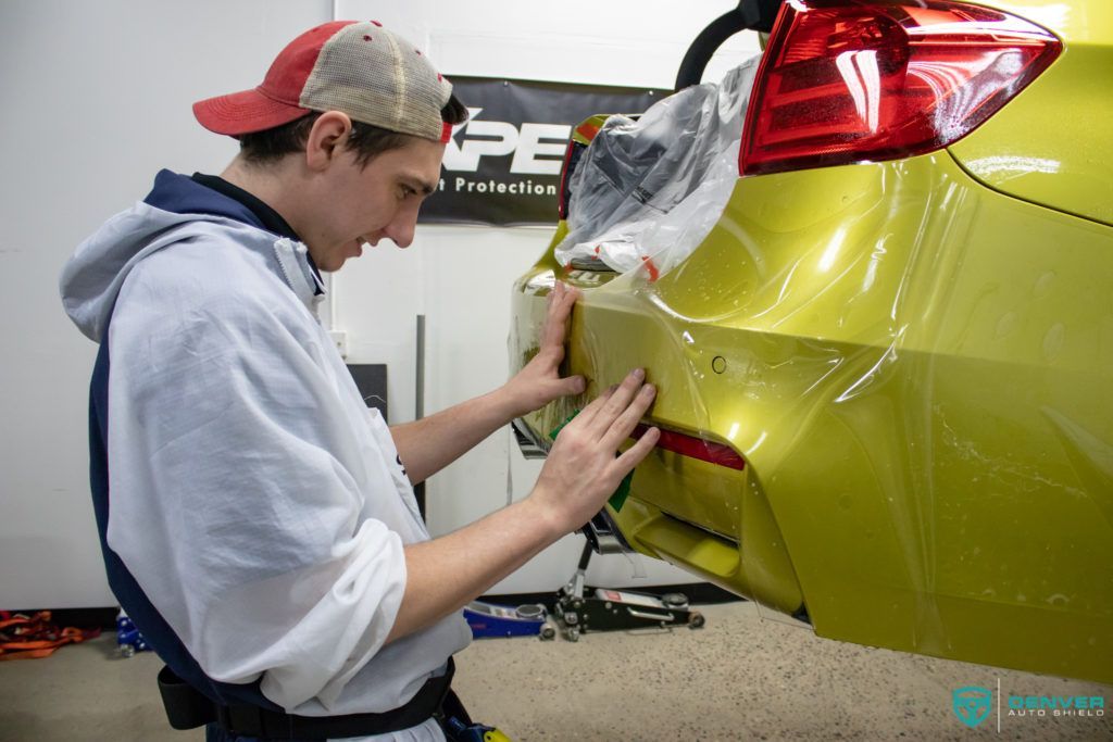 A man is wrapping a yellow car with plastic wrap.