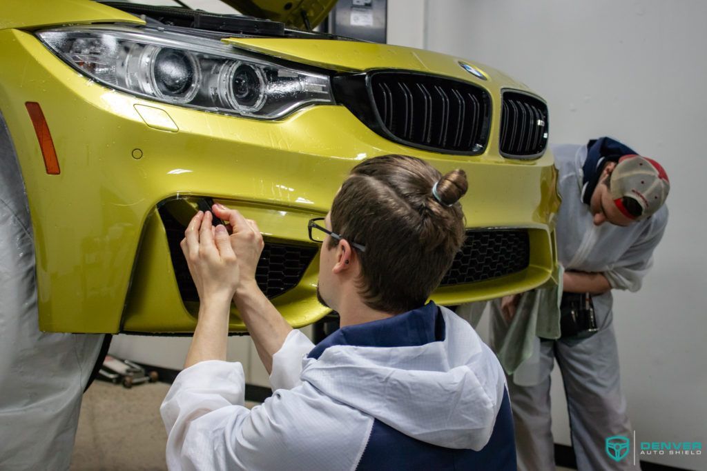 Two men are working on a yellow bmw m3 in a garage.