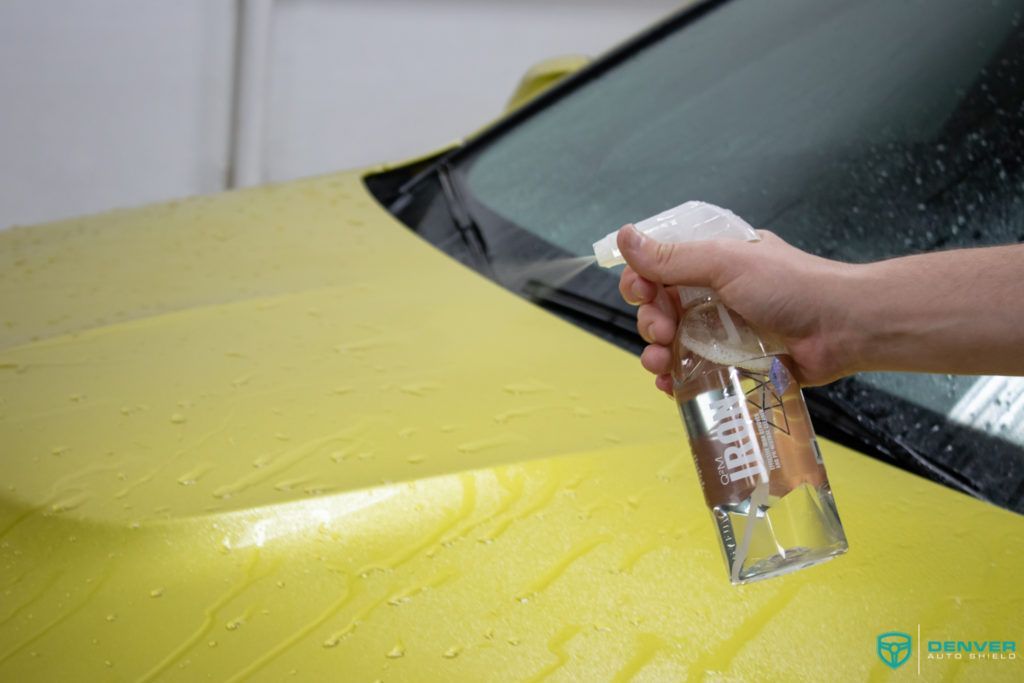 A person is spraying water on a yellow car.