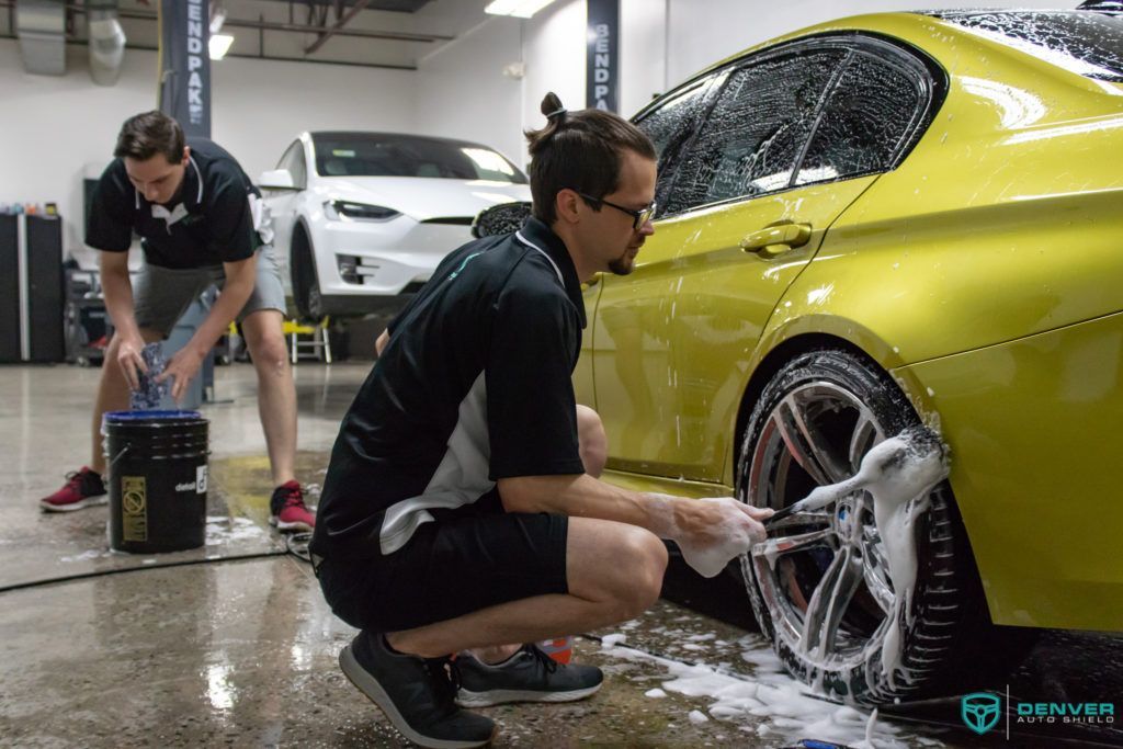 Two men are washing a yellow car in a garage.