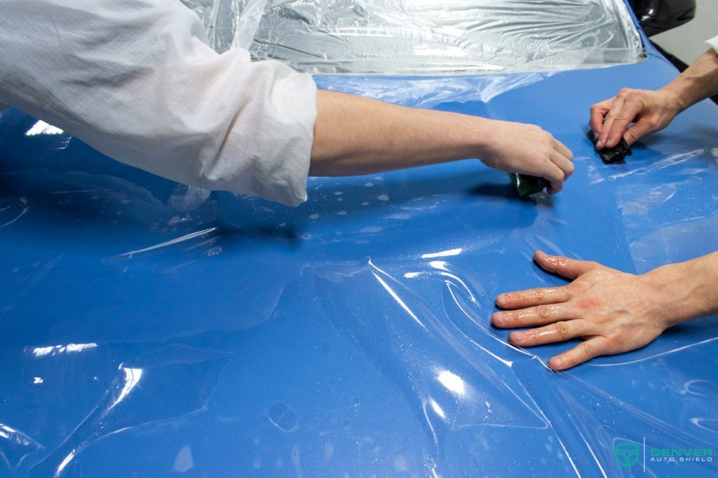 Two people are wrapping a blue car with plastic wrap.