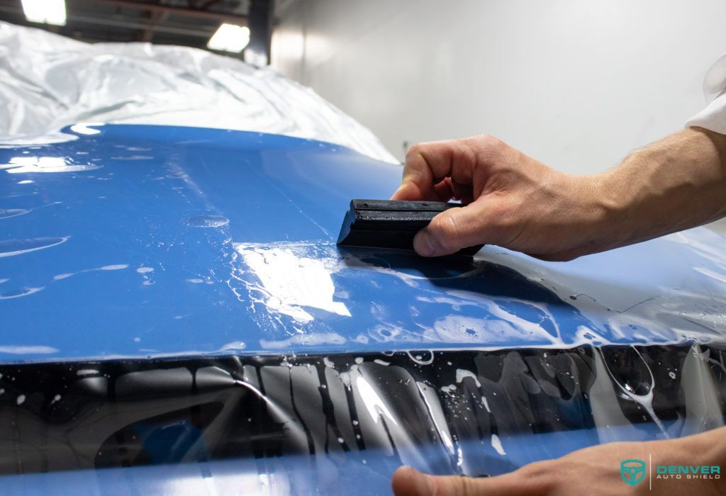 A person is wrapping a blue car with plastic wrap.