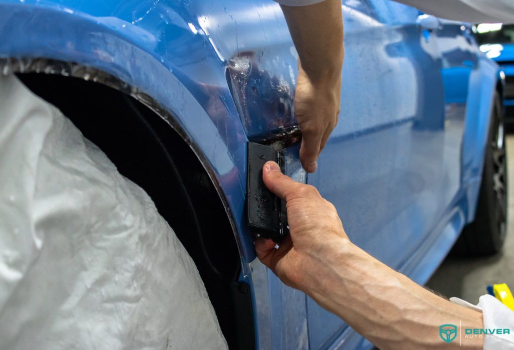 A person is wrapping a blue car with plastic wrap.