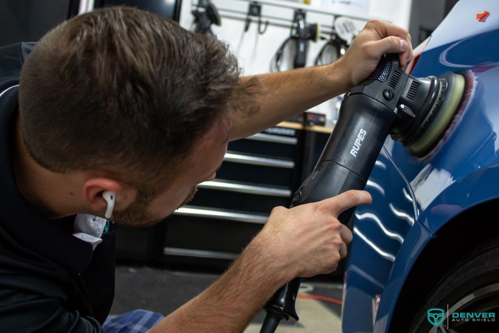 A man is polishing a blue car with a machine.