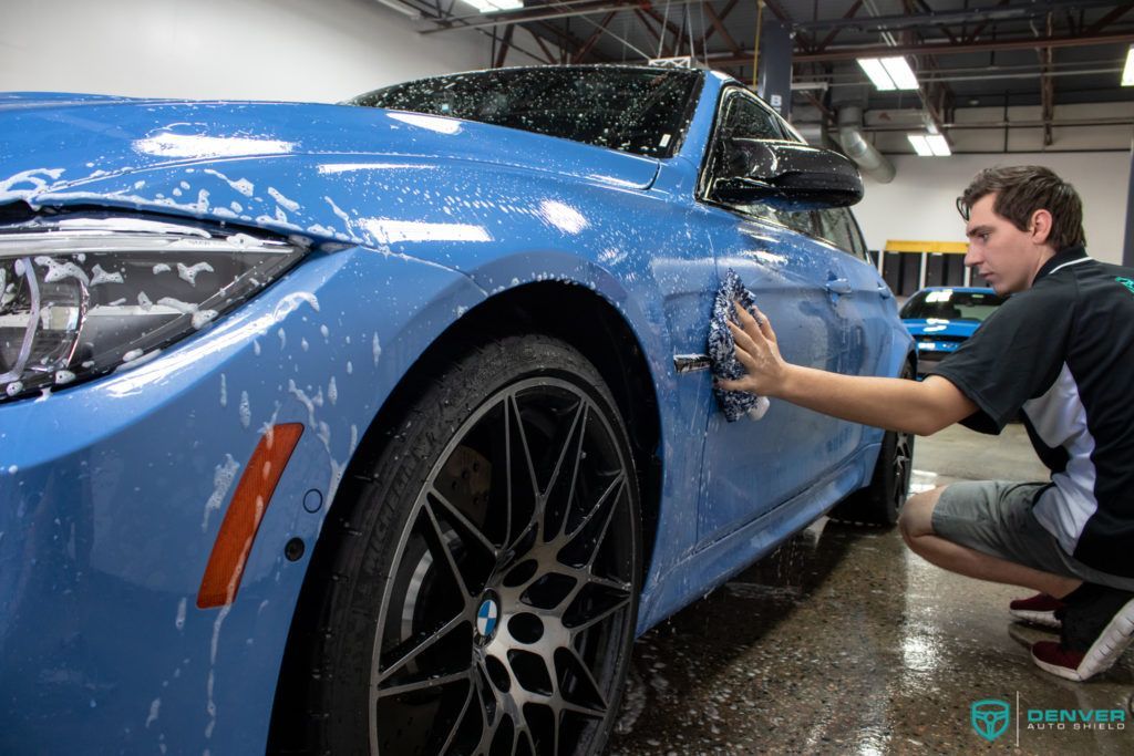 A man is washing a blue bmw m3 in a garage.