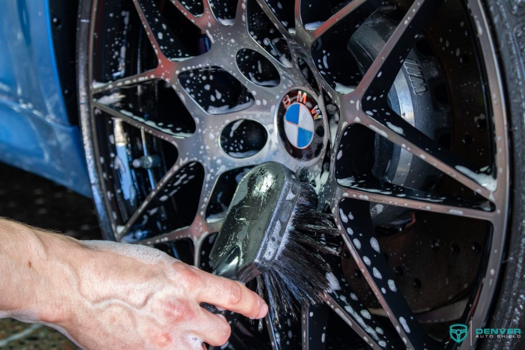 A person is washing a bmw wheel with a brush.