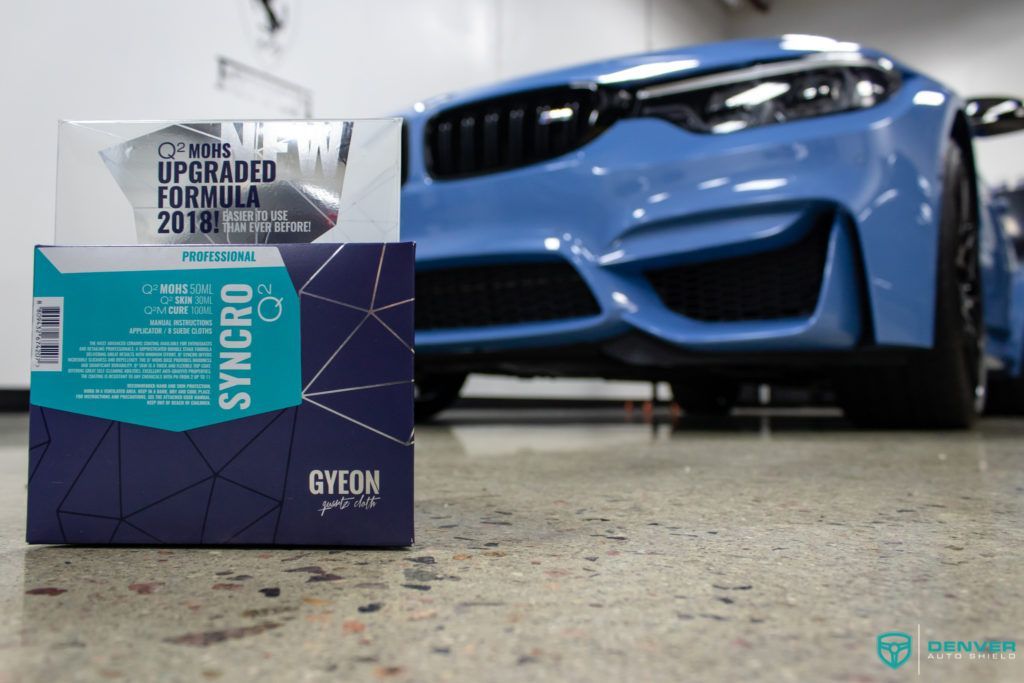 A blue bmw m3 is parked in a garage next to a box of gyeon products.