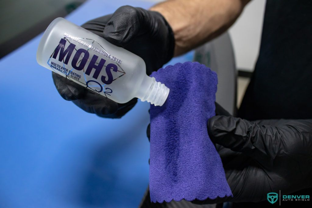 A person is holding a bottle of mohs and a purple cloth.