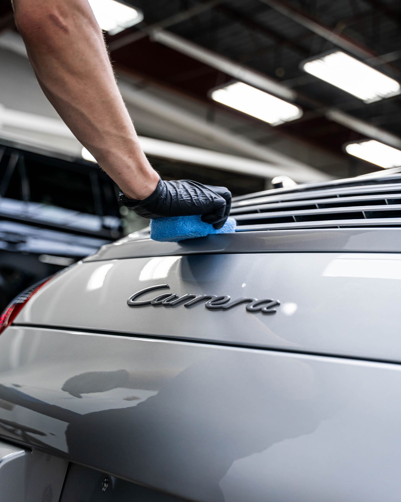 A person is cleaning the back of a silver porsche carrera with a sponge.