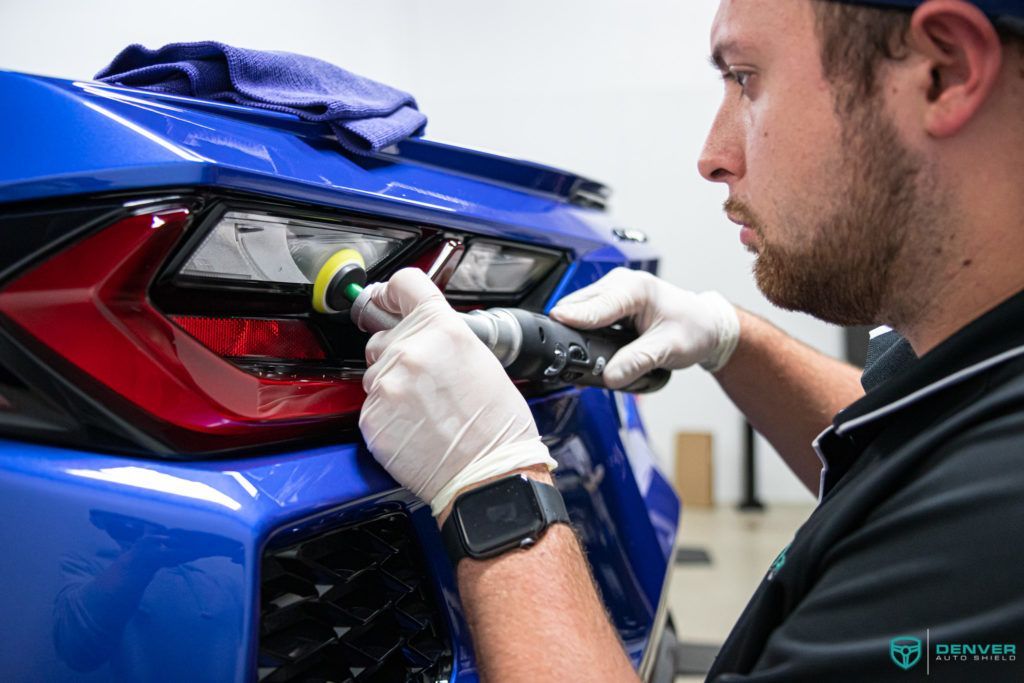 A man is polishing the tail light of a blue car.