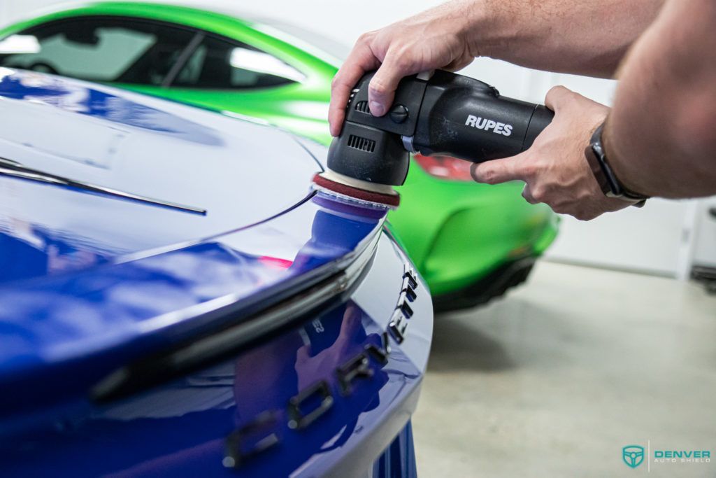 A man is polishing a blue car with a machine.