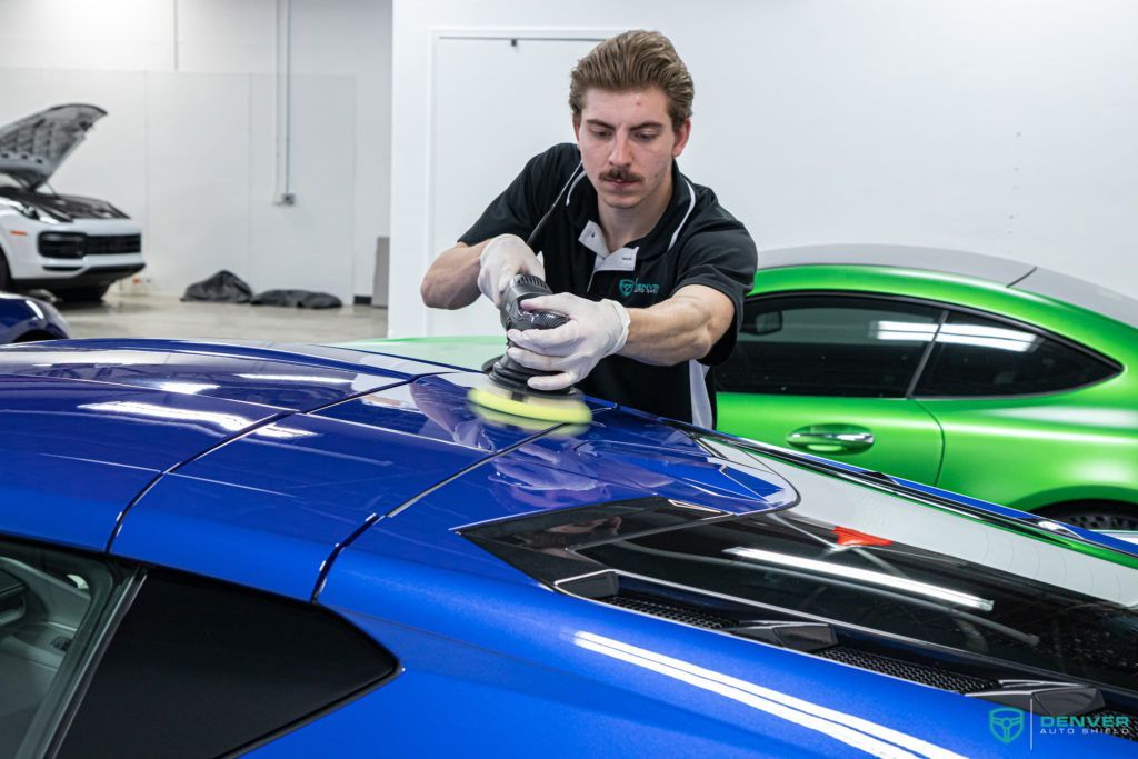 A man is polishing the hood of a blue car.