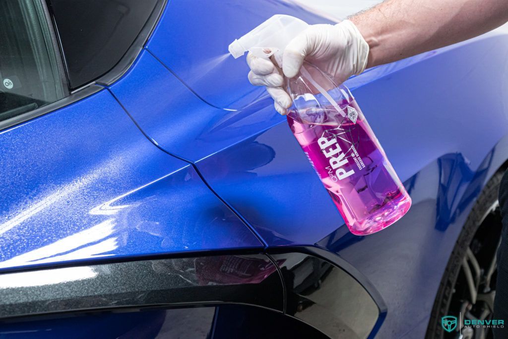 A person is cleaning a blue car with a spray bottle.