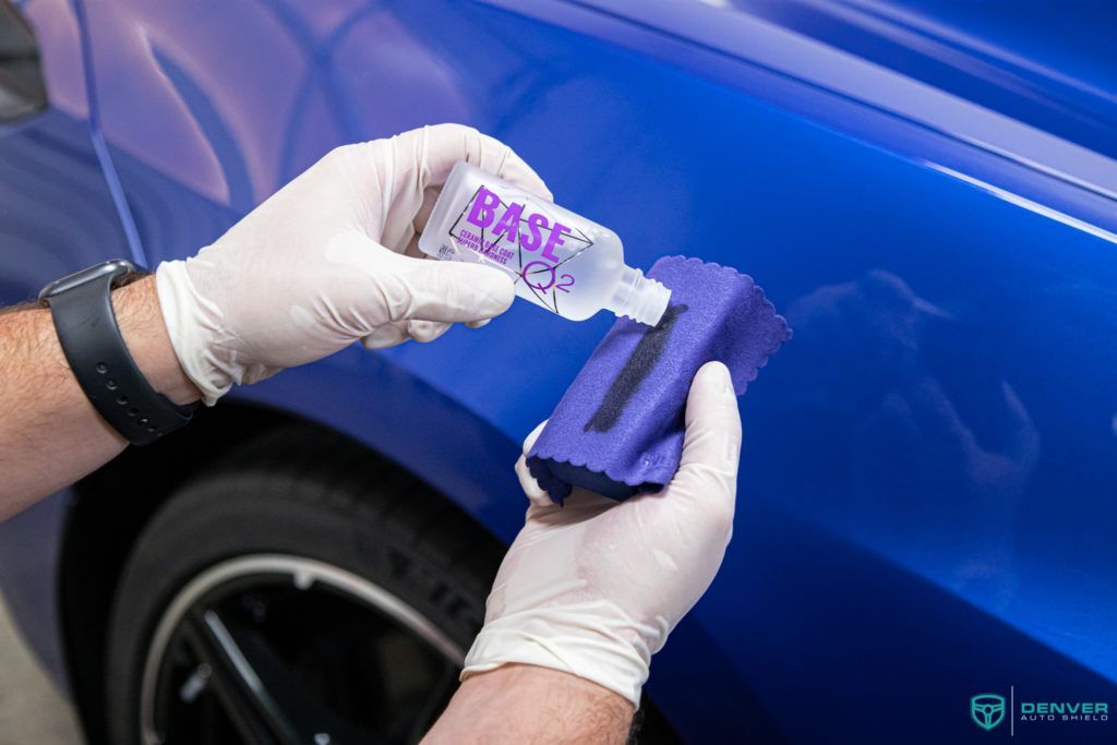 A person is applying wax to a blue car with a sponge.