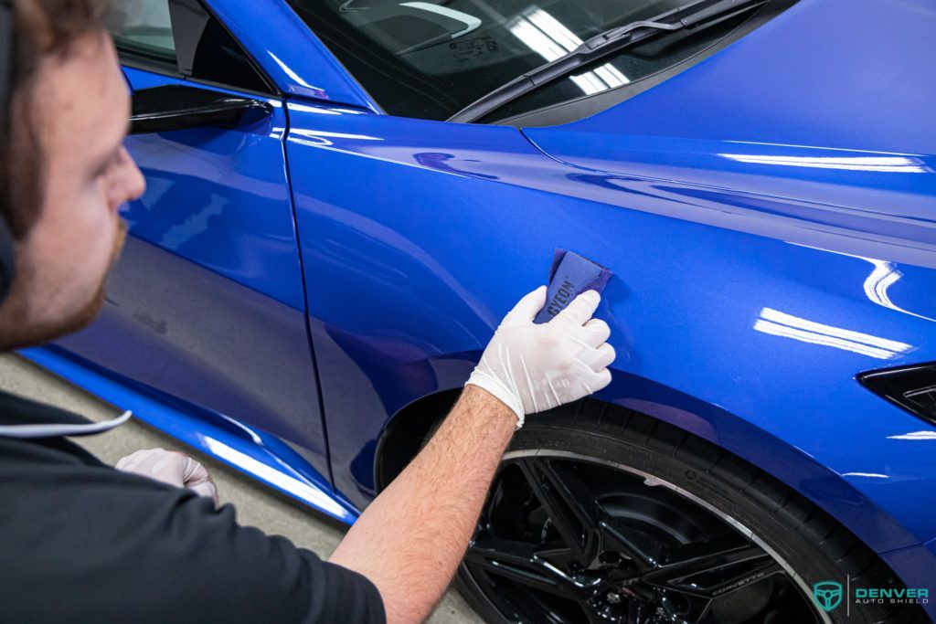 A man is polishing the fender of a blue car.