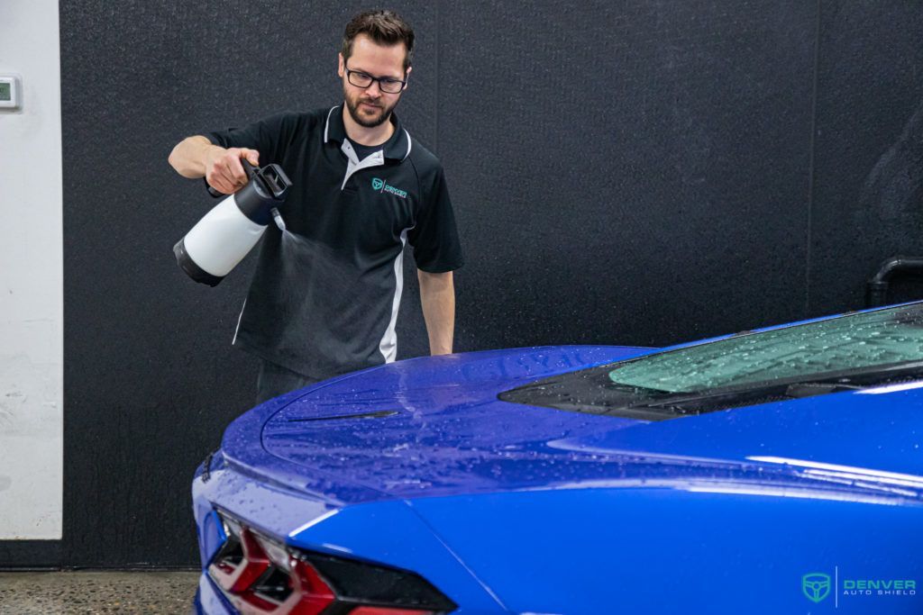 A man is spraying a blue car with a spray bottle.