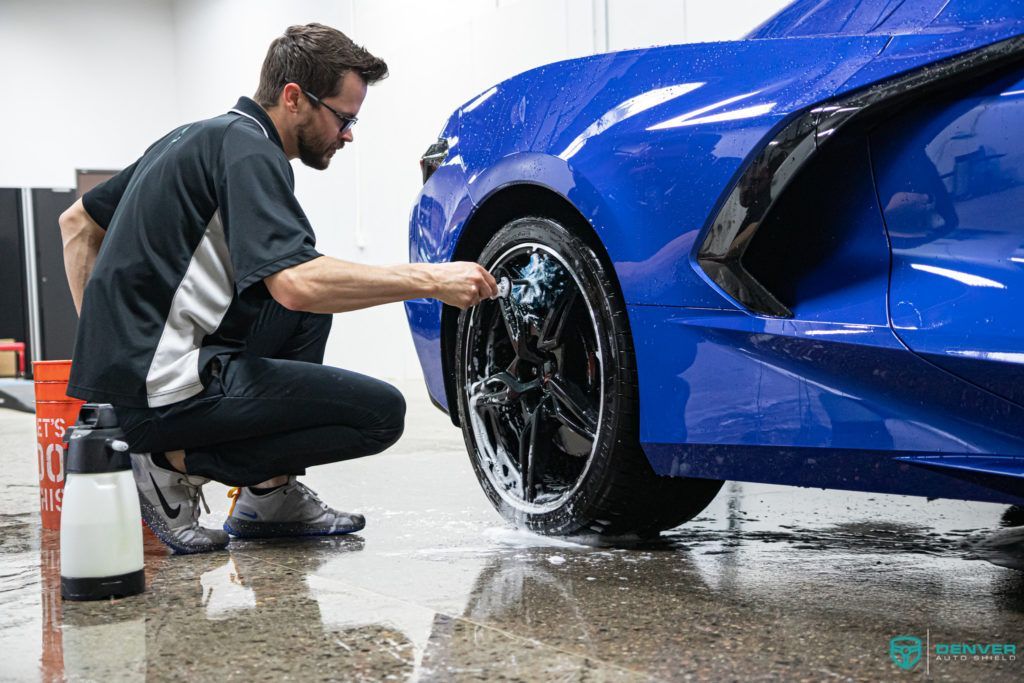 A man is cleaning the wheels of a blue sports car.