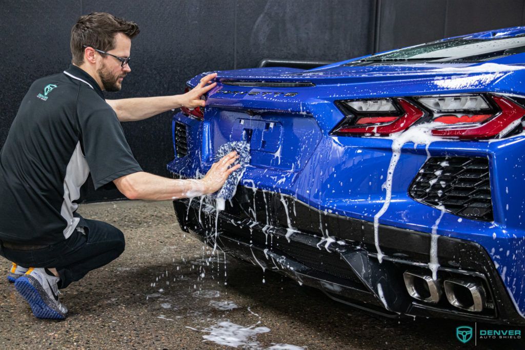 A man is kneeling down to wash a blue sports car.