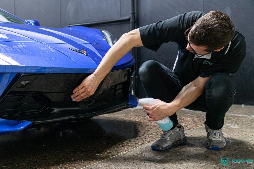 A man is cleaning the front bumper of a blue sports car.