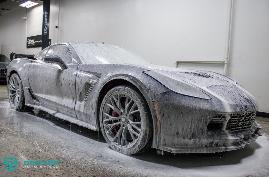 A black corvette is covered in foam in a garage.