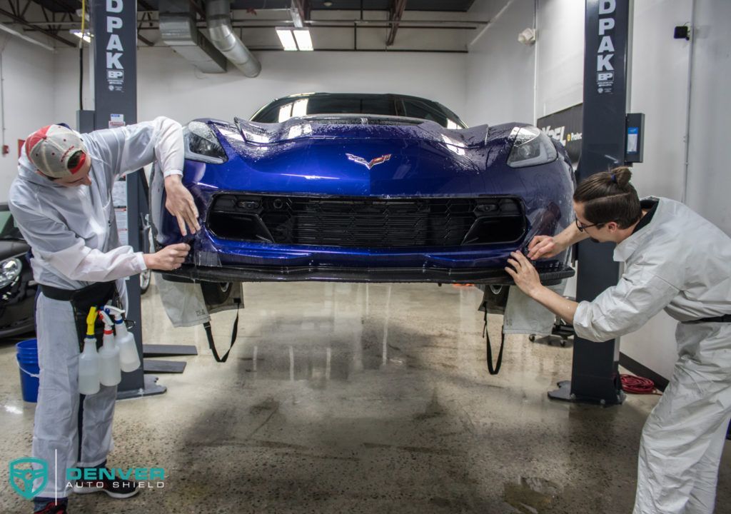 Two men are working on a blue car in a garage.