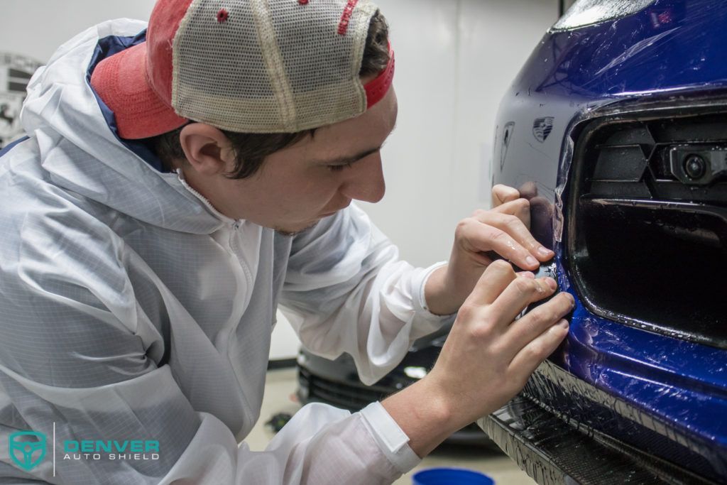 A man is wrapping a blue car with a blue tape.