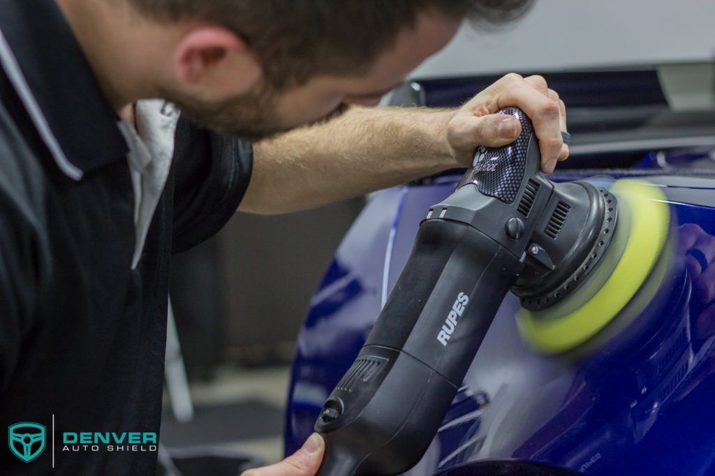 A man is polishing a blue car with a polisher.