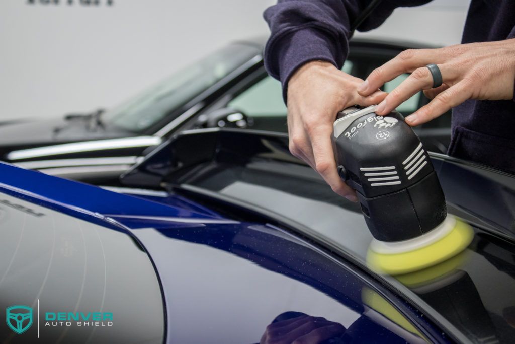 A person is polishing a blue car with a machine.