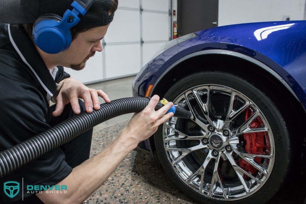 A man wearing headphones is using a vacuum cleaner to clean a car wheel.