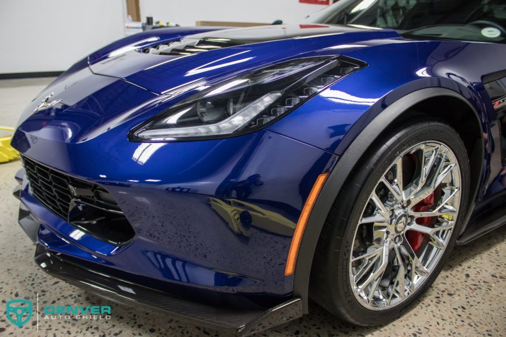 A blue sports car with chrome wheels is parked in a garage.