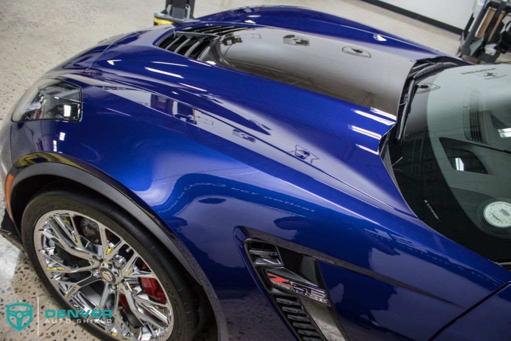 A blue sports car with a black hood is parked in a garage.