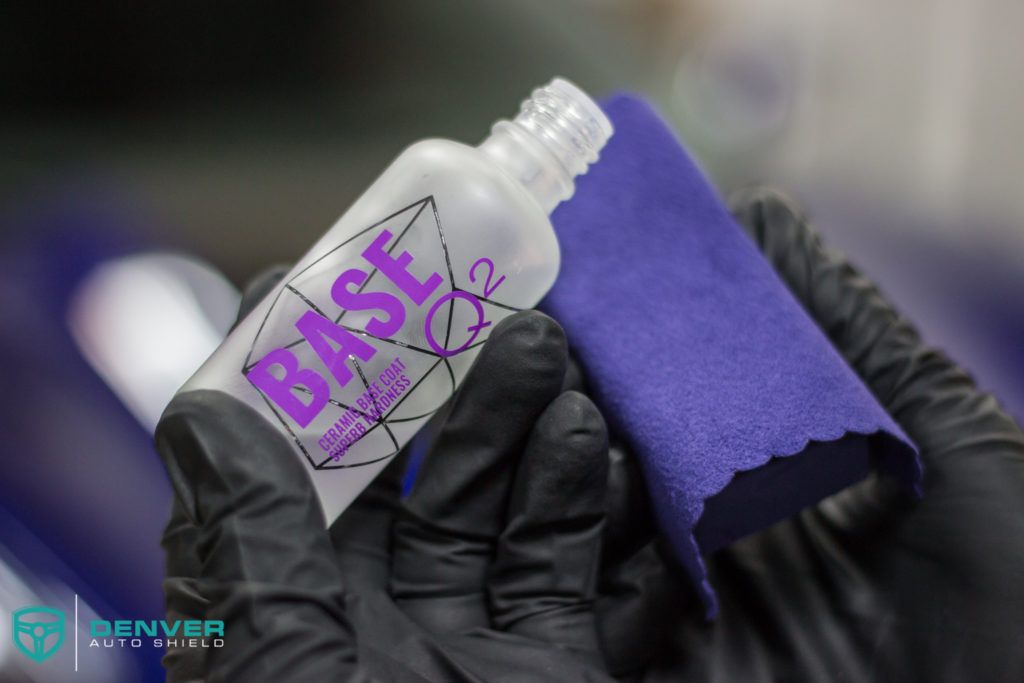 A person wearing black gloves is holding a bottle of base and a purple cloth.