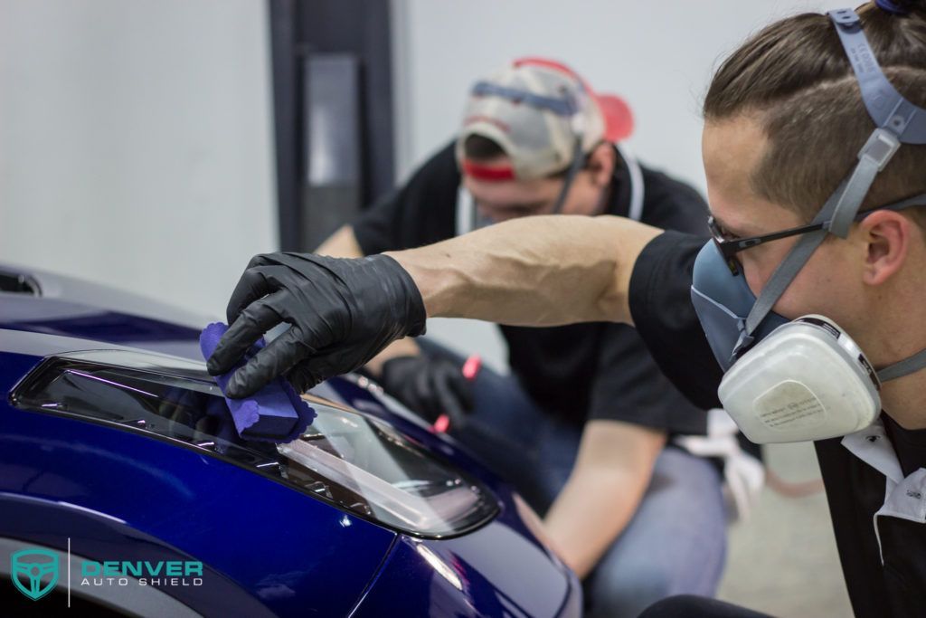 A man wearing a mask is working on a car.