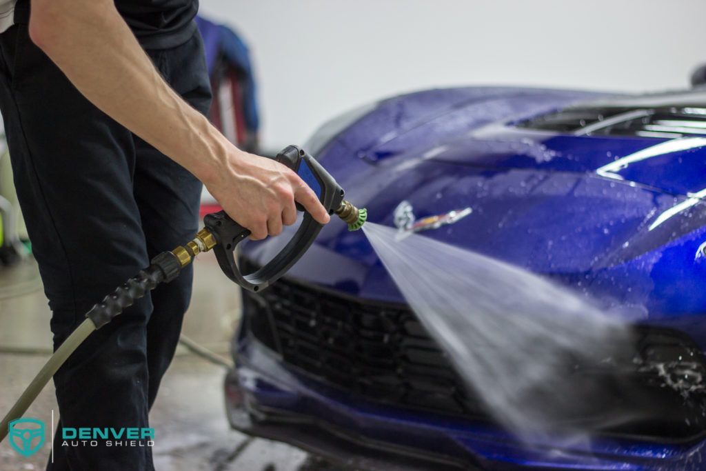 A man is washing a blue car with a hose.