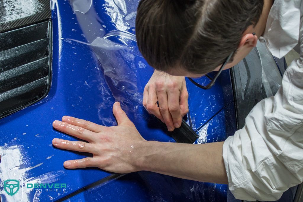 A person is wrapping a blue car with a clear film.