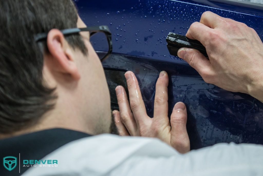 A man wearing glasses is looking at a blue car with a flashlight.