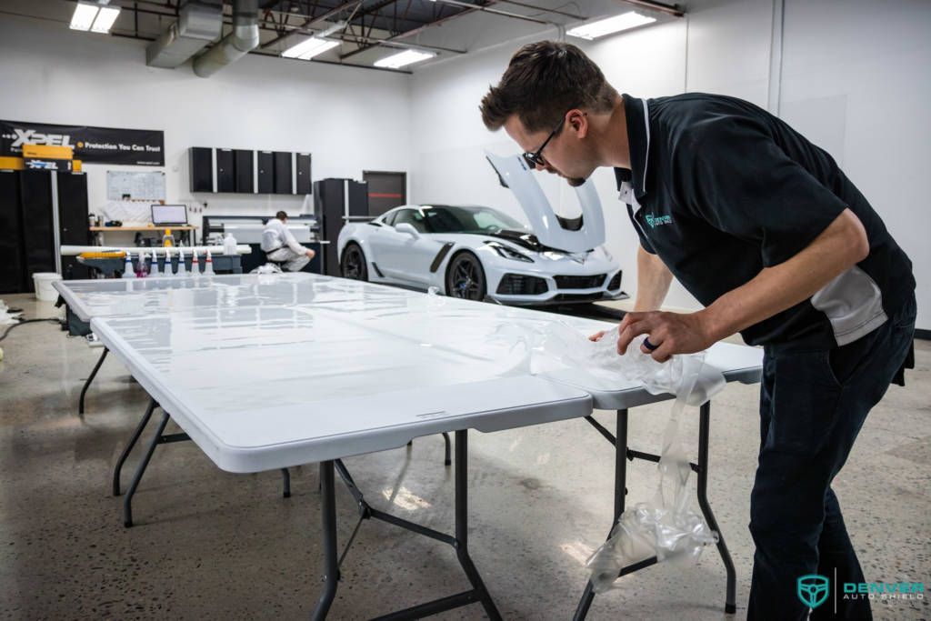 A man is working on a table with a car in the background.