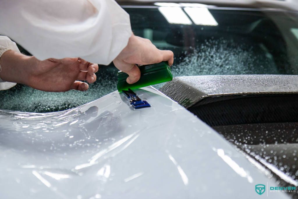 A person is applying a clear plastic film to a car hood.