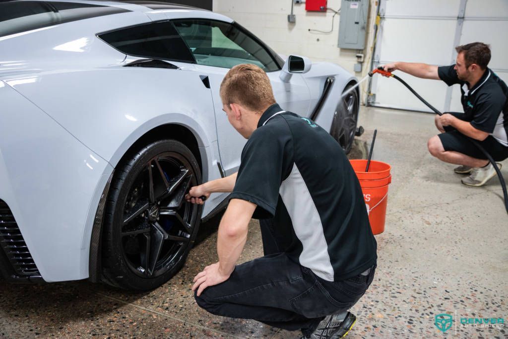 Two men are cleaning a white sports car in a garage.