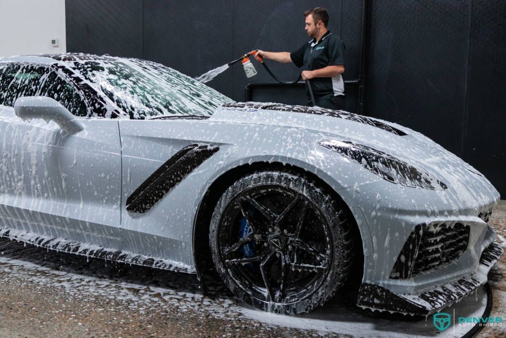 A man is washing a white sports car with foam.