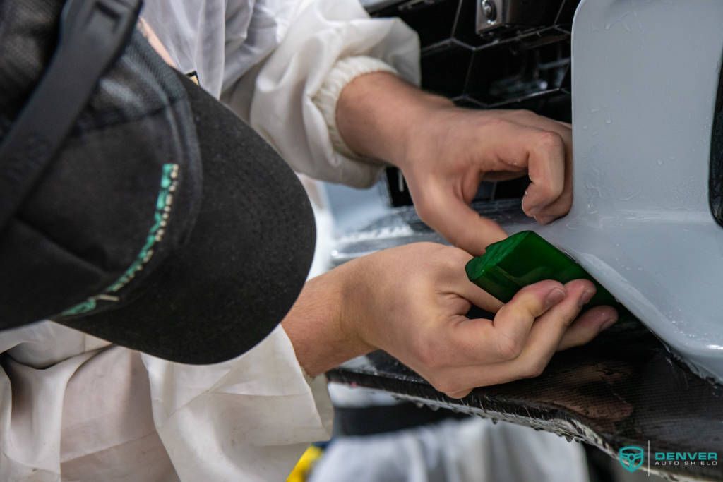 A man wearing a black hat is working on a car bumper.