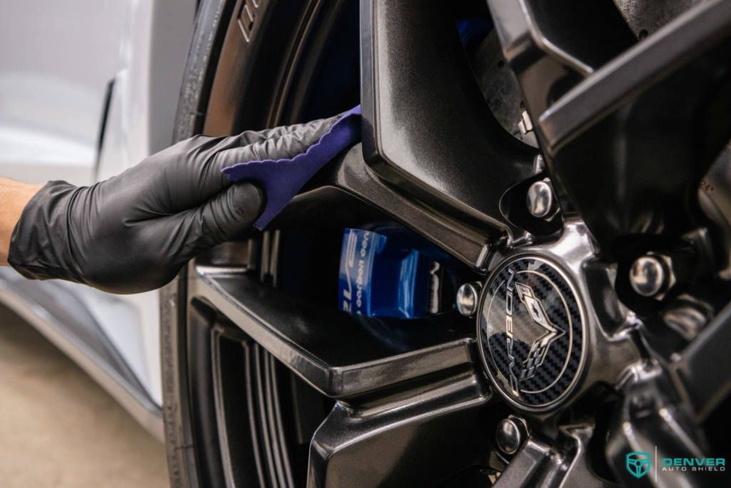 A person wearing black gloves is cleaning a car wheel with a cloth.