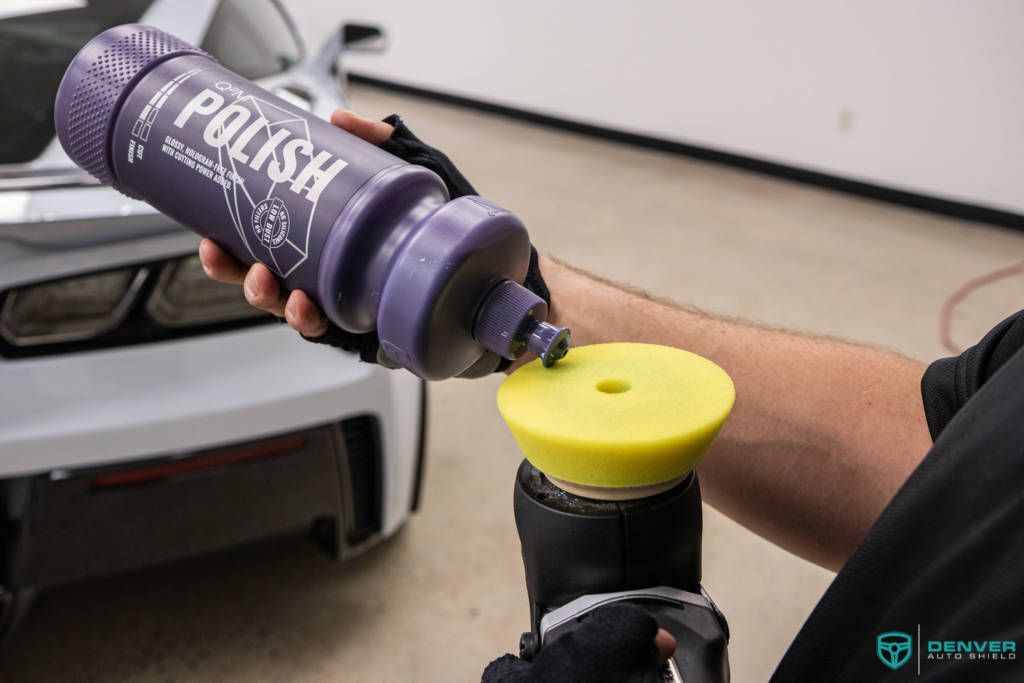 A person is polishing a car with a bottle of polish.