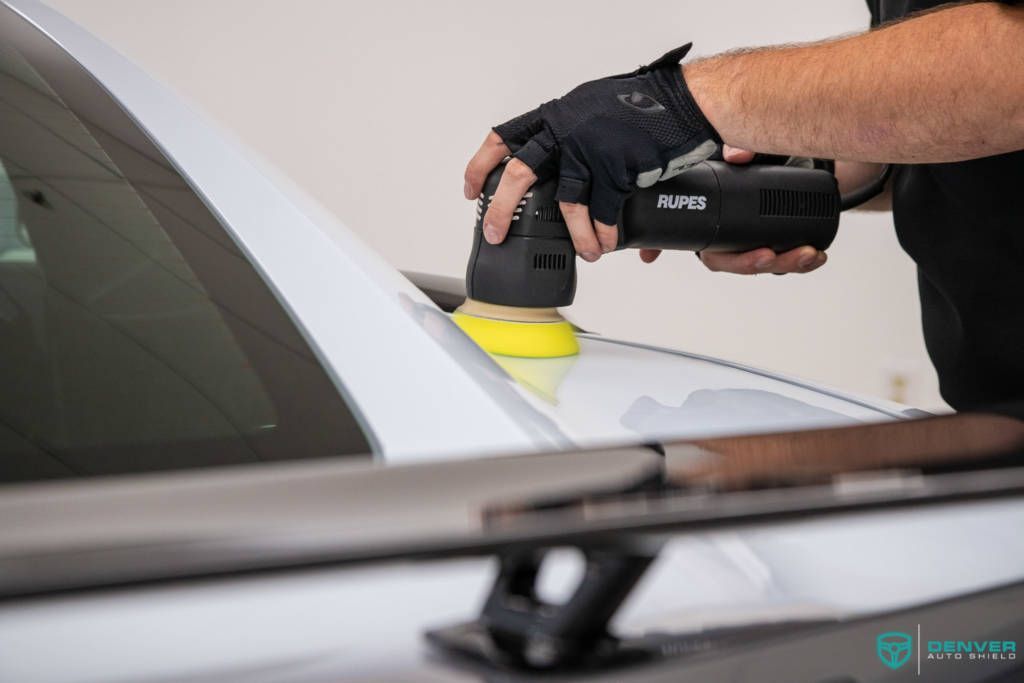 A man is polishing a white car with a machine.